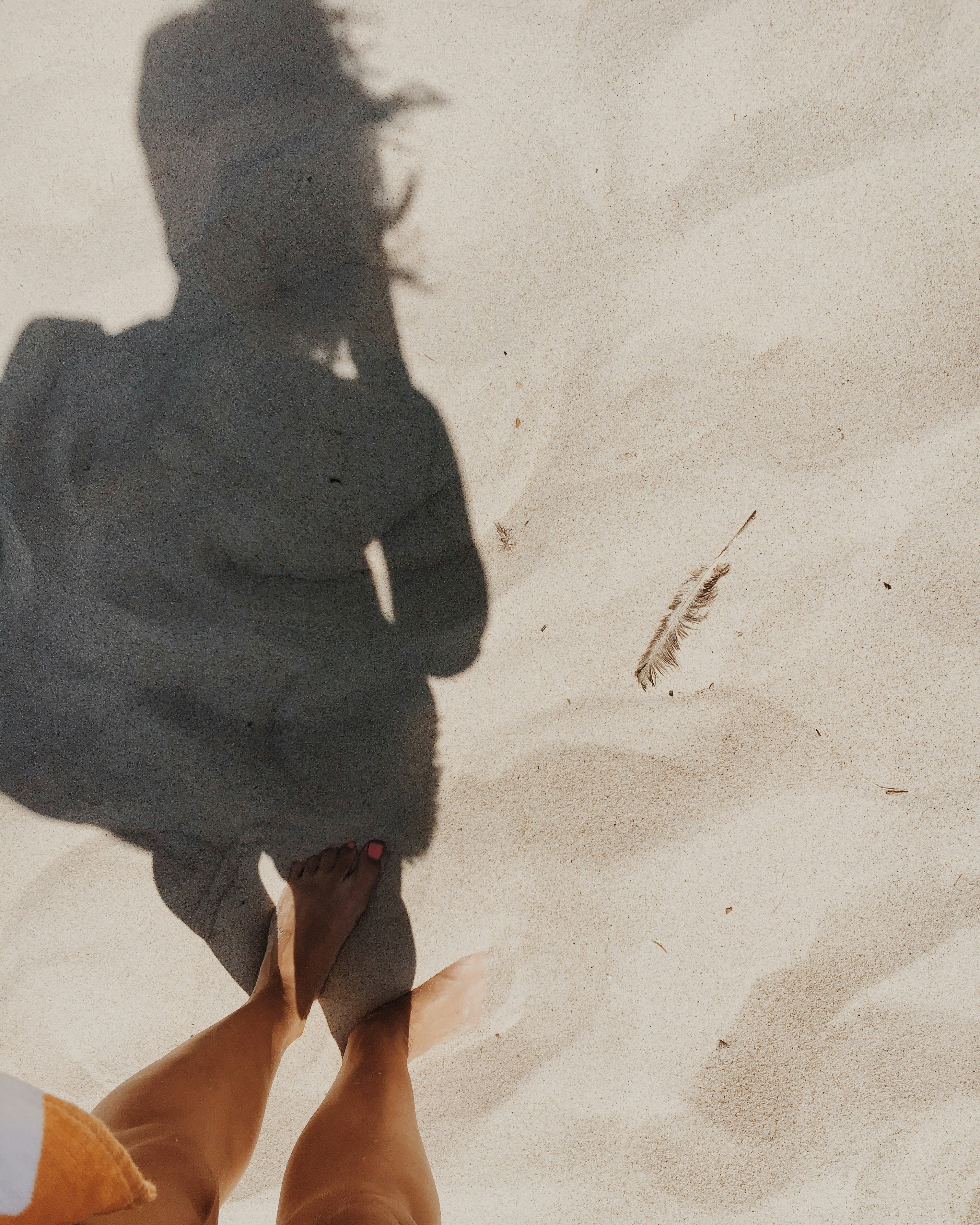 The shadow of a woman standing in the sand on a beach.